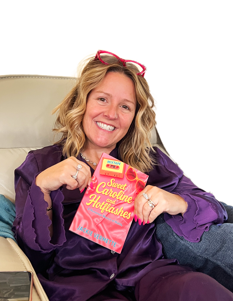 Jackie Vermette holding a copy of her book wearing a purple top smiling in the camera